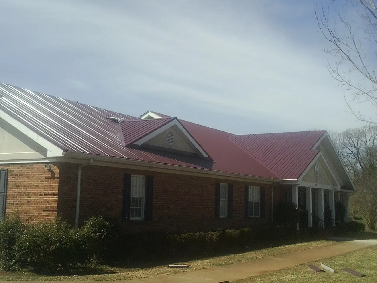 Red metal roof with gabled entries on a long brick building, from a Hail Damage Roof Repair job in Fate