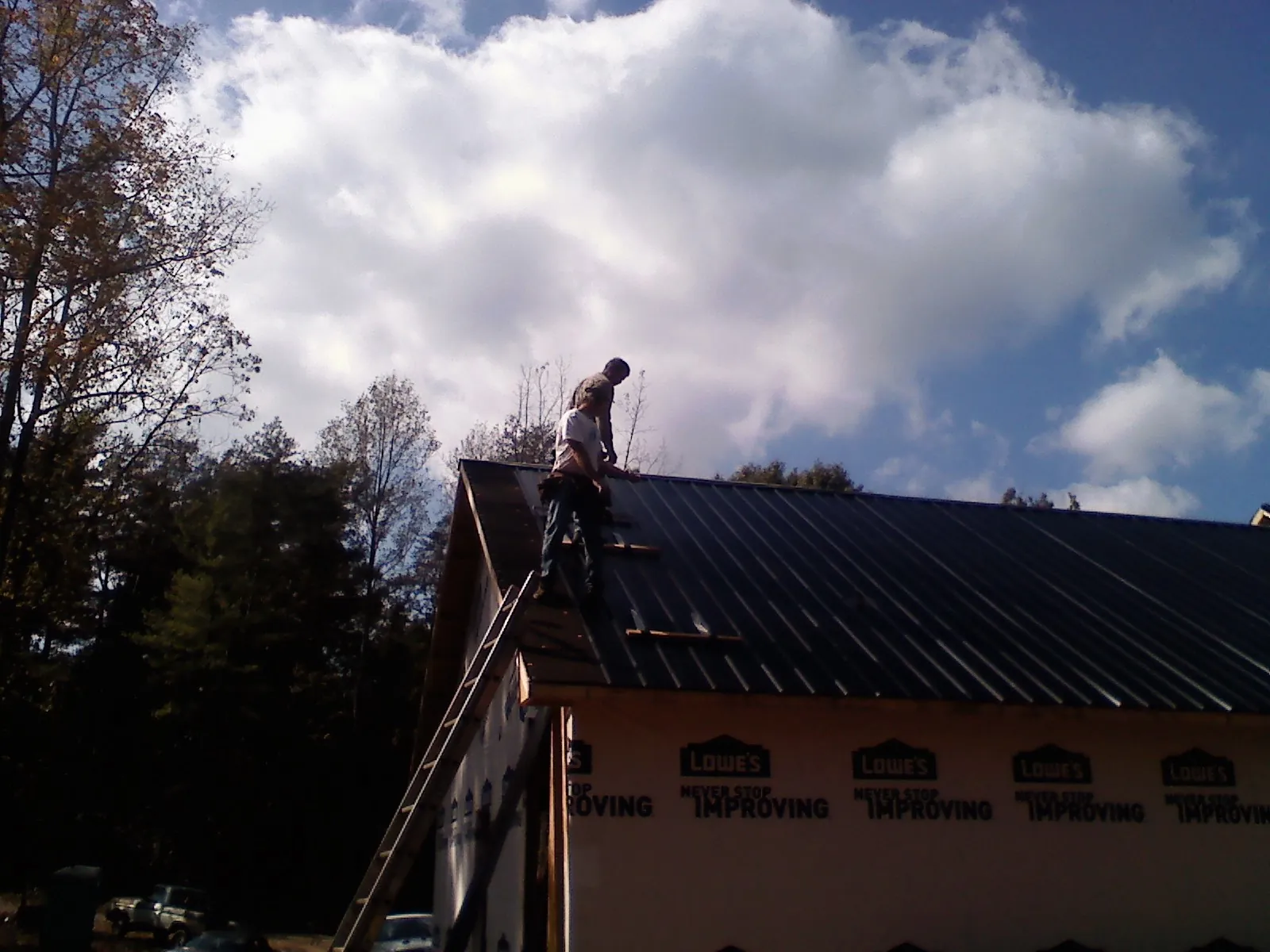Roofer fastening dark metal panels high against a cloudy sky, from a Roof Inspection job in Fate