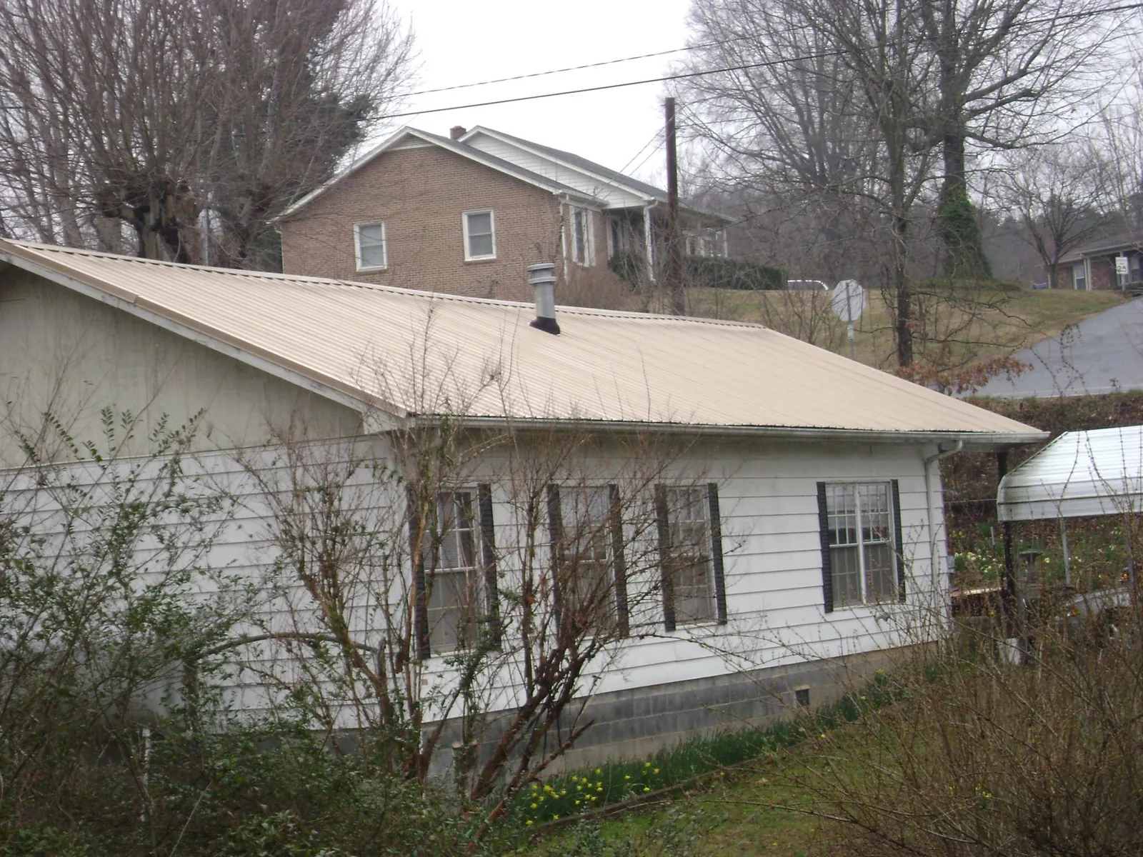 Tan metal roof on a white sided house set into a hillside — Commercial Roofing by Roofing Brothers in Fate